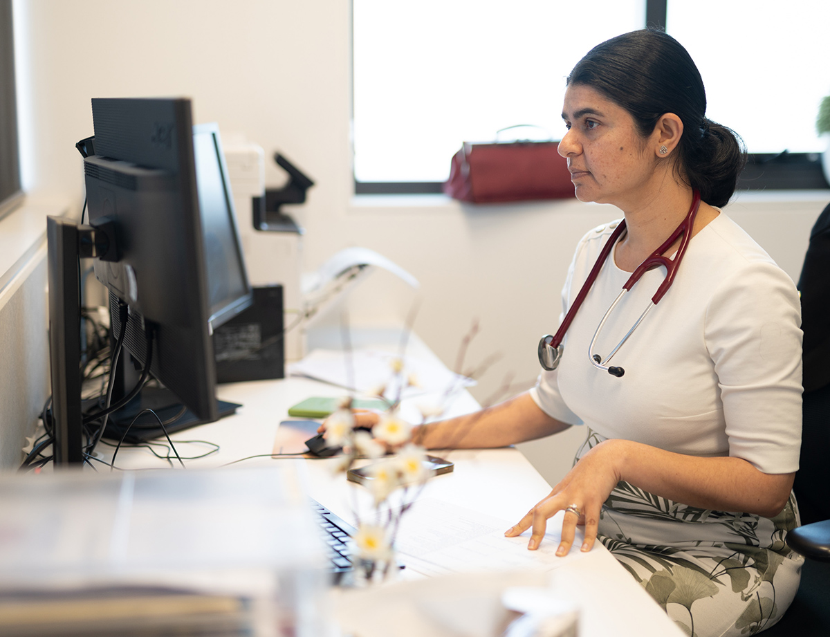 Dr Vicka Poudyal at her desk wearing a stethoscope working on her computer.
