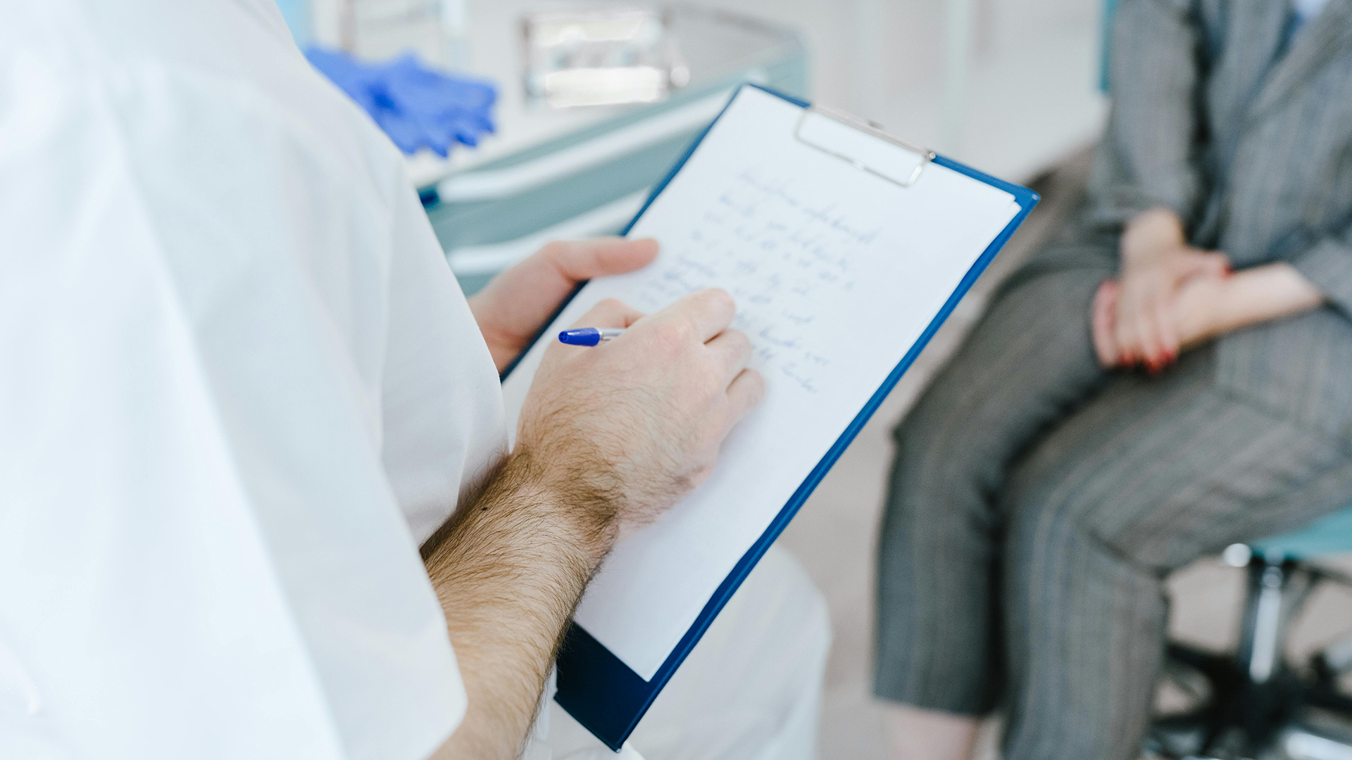 Doctor writing on paper whilst having a patient consultation.