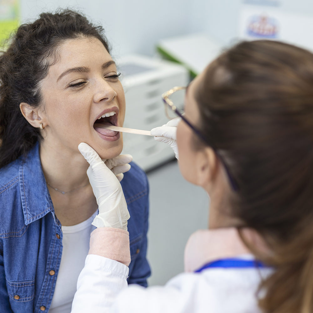 Clinician examining a patient’s throat using a tongue depressor.