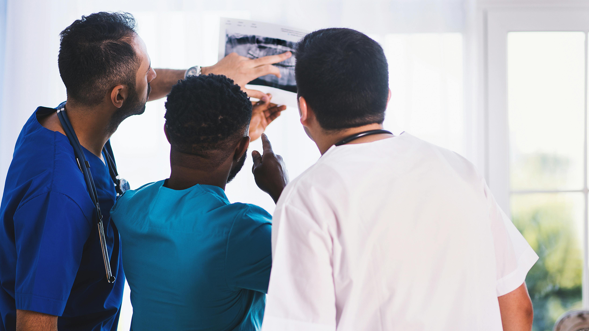 Three doctors looking at a jaw X-ray showing teeth.