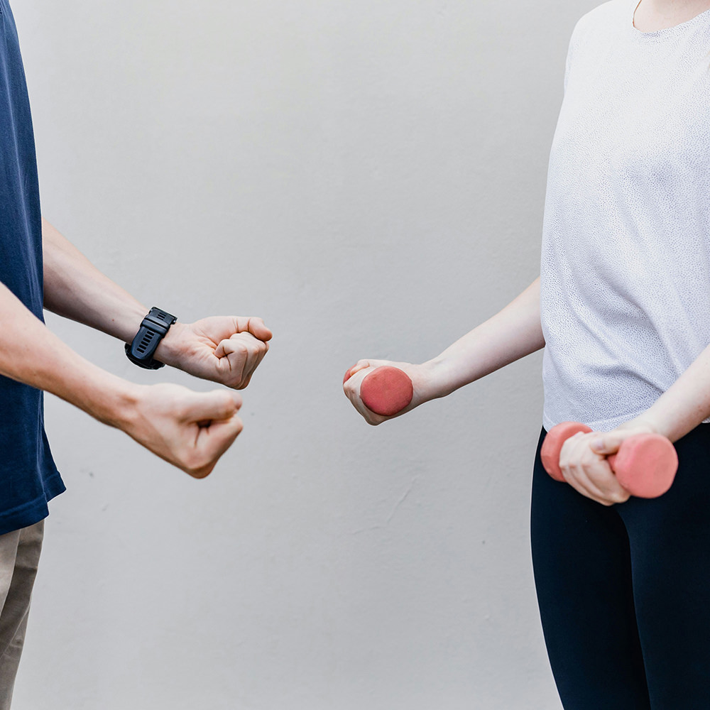 Male physiotherapist instructing female patient on how to do bicep curls with light weights.
