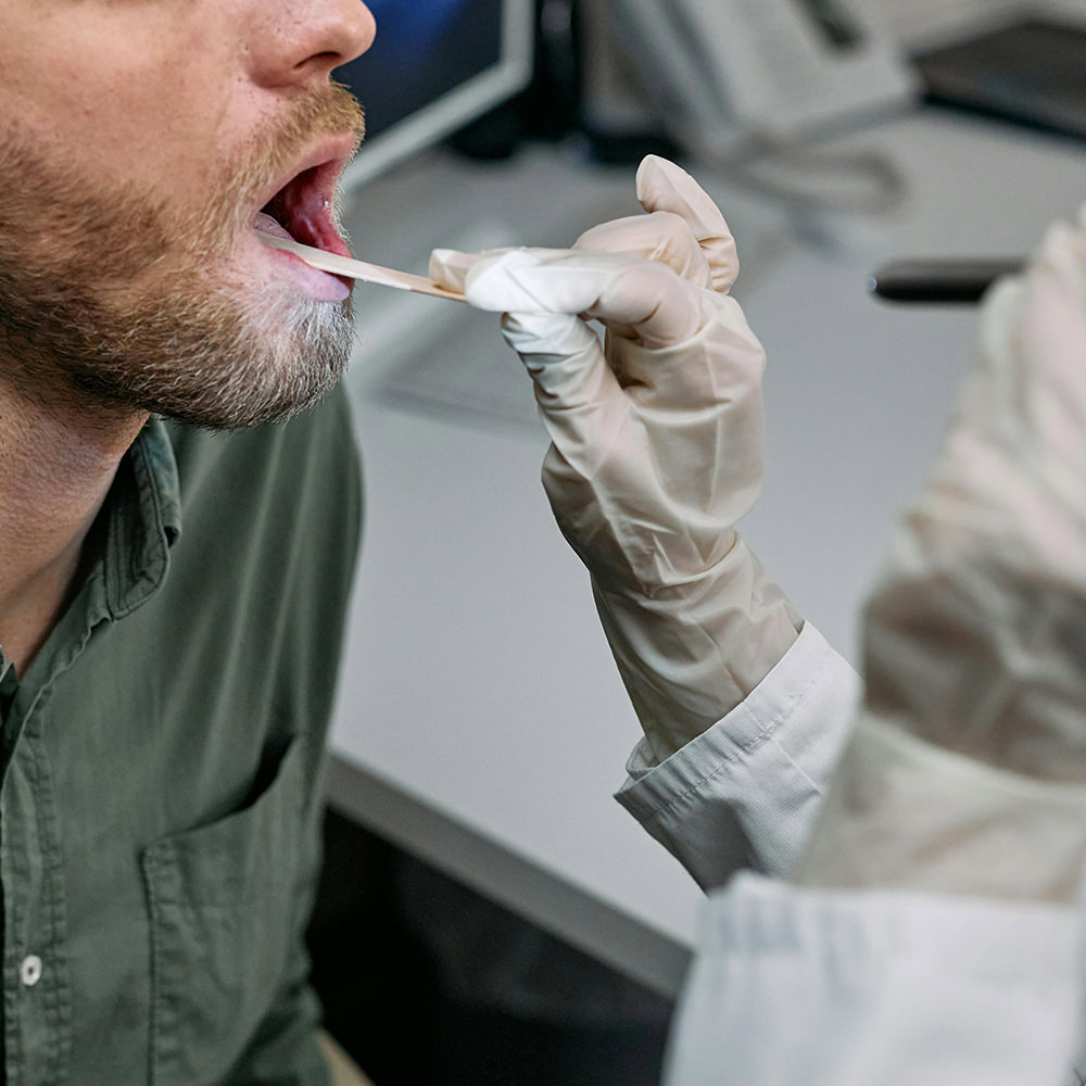 Clinician examining a patient’s throat using a tongue depressor.